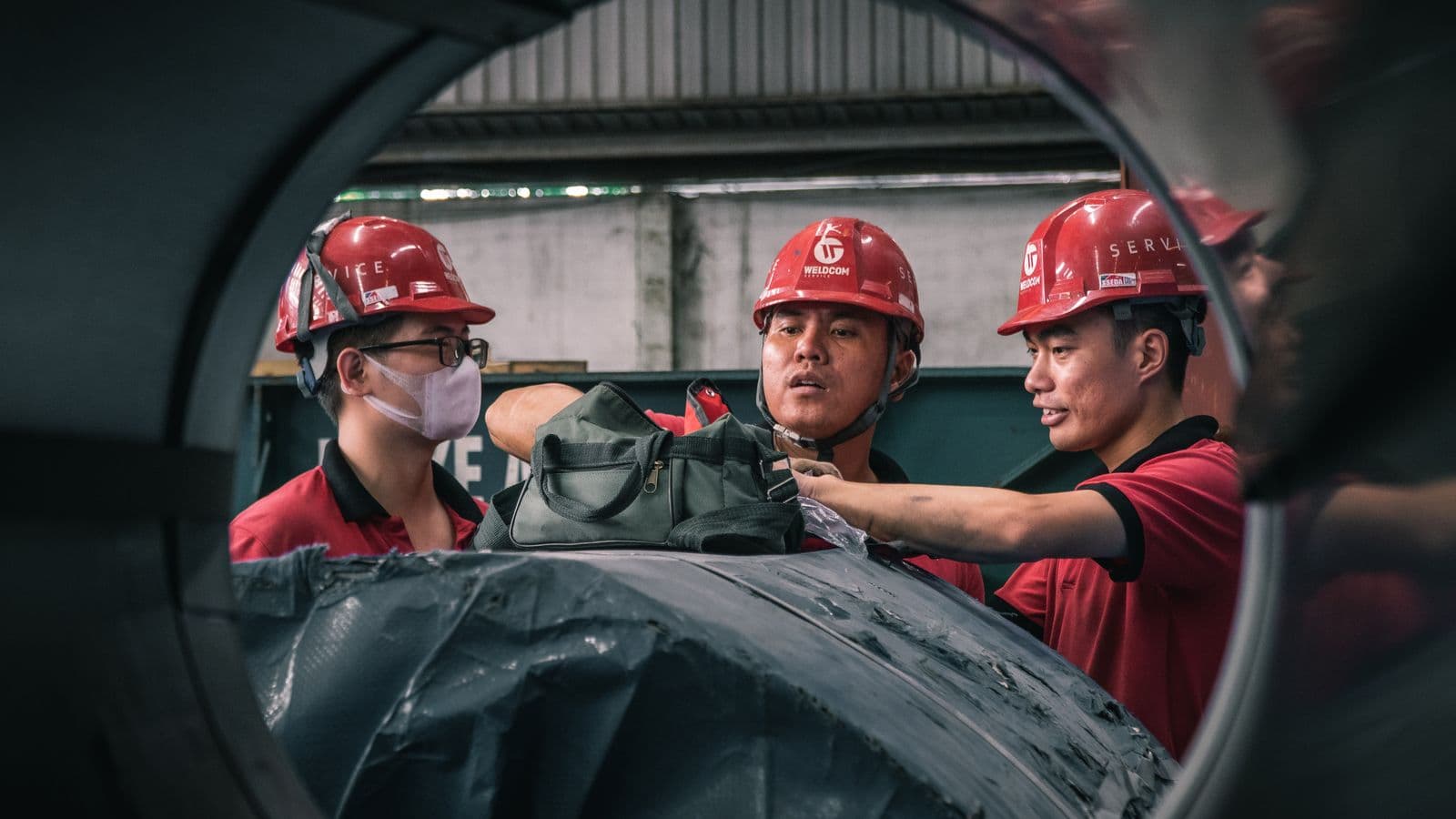 Three fitters in hard hats working on a pipe section, with the missing vest picked up as an alert