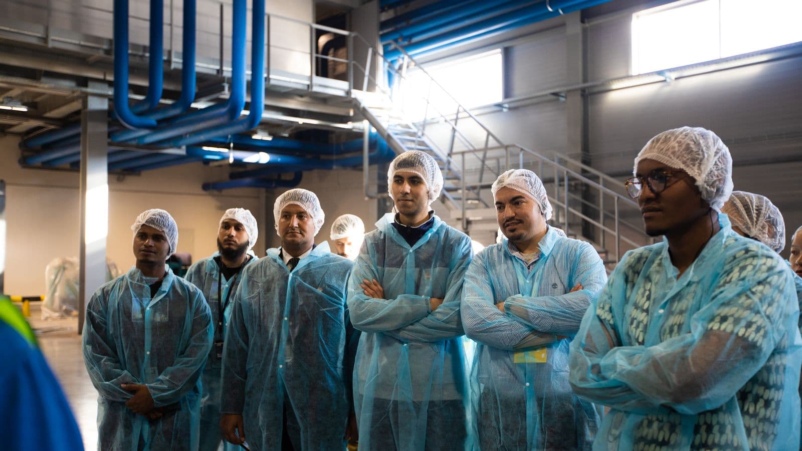 Workers in plant coveralls and hairnets at the start of a shift, five faces matched to a name and three marked unknown